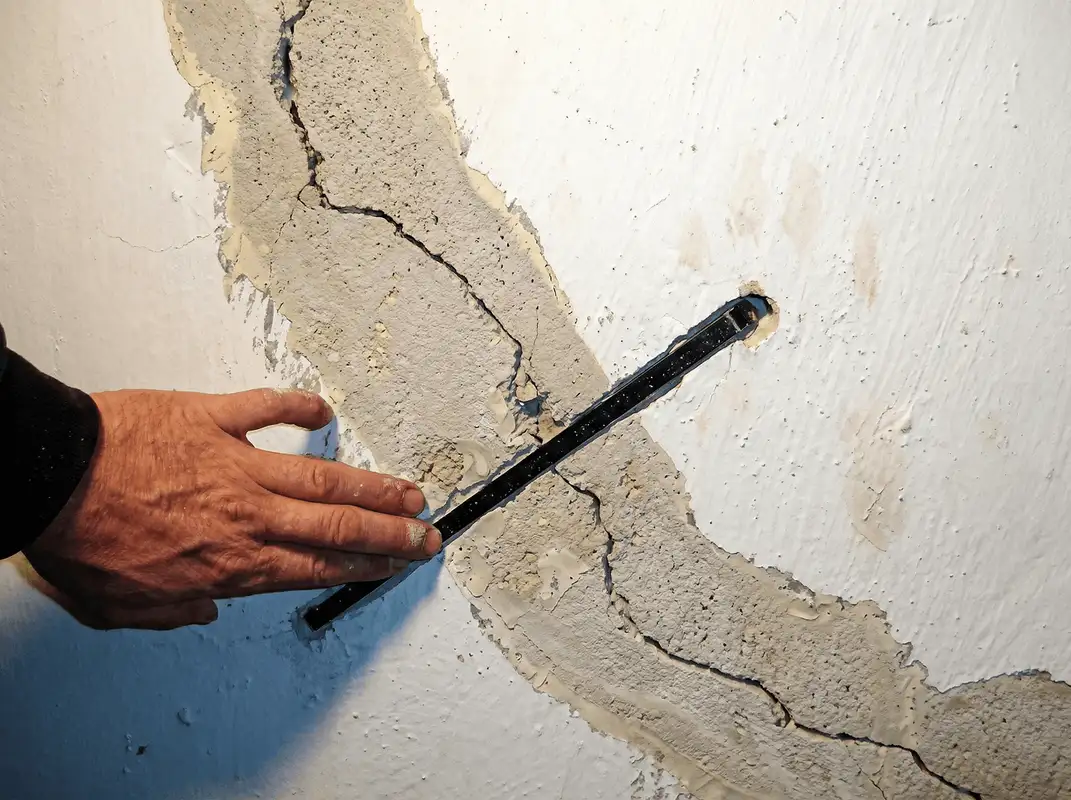 A wall with a large crack is being inspected by a professional in Lowell, MA